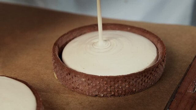 Chef adding white cream to the small tarts with chokolate