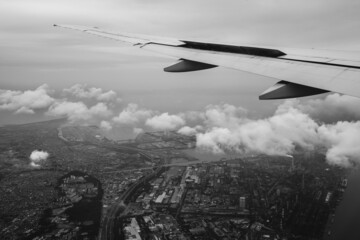 Wing of plane flying over the clouds and the city of Tokyo, Japan (in black and white)
