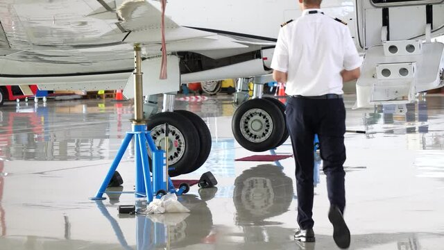 Pilot walks towards jet airplane on jacks during maintenance in hangar