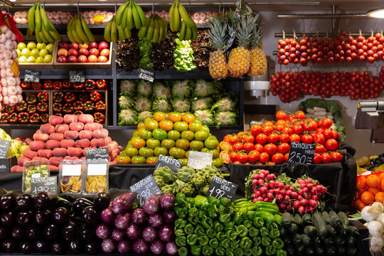 Colorful market counter with large assortment of fruits and vegetables. Price tags with product names in Catalan