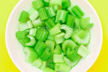 Fresh Chopped Celery Pieces with Water Drops in White Bowl on Yellow Background. Vegan and...