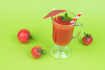Fresh tomatoes and a glass glass with tomato juice on a green background.