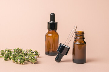 A branch of medicinal herbs and vials with an eyedropper on a beige background.