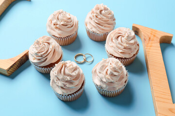 Tasty cupcakes and wedding rings on color background