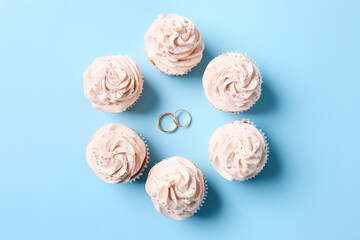Tasty cupcakes and wedding rings on color background