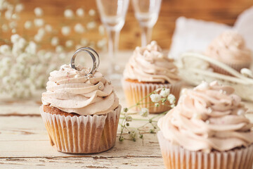 Tasty cupcake with wedding rings on white wooden background