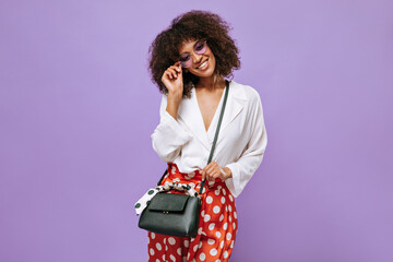 Modern lady in polka dot pants and glasses smiling on isolated background. Curly girl in light...