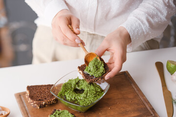Woman making tasty toast with pesto sauce on table, closeup