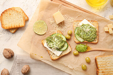 Tasty toasts with pesto sauce and olives on light background