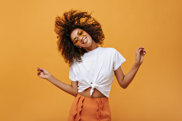 Emotional curly girl in light t-short playing her hair on isolated backdrop. Joyful woman in...