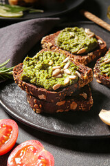 Tasty toasts with pesto sauce on dark background, closeup