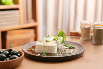 Plate of tasty feta cheese with spices on table in kitchen