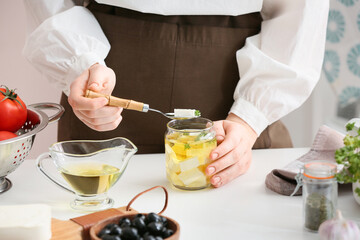 Woman taking piece of tasty feta cheese from jar on table in kitchen, closeup