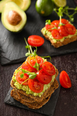 Tasty bruschettas with tomato and guacamole on dark background, closeup