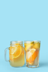 Glass and mason jar of lemonade on color background