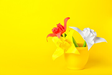 Pot with origami daffodils on color background