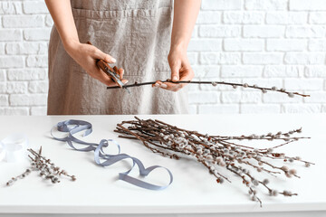 Woman making bouquet of willow branches near brick wall