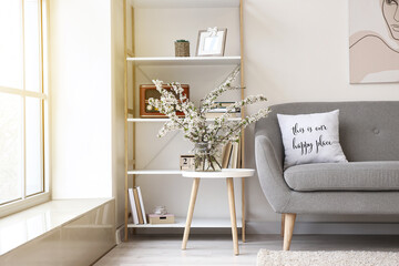 Vase with blossoming branches and book shelf in interior of modern room