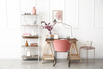 Modern workplace with vase and blossoming branches near light wall