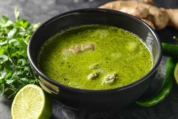 Bowl of tasty green chicken curry and ingredients on grunge background, closeup