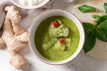 Bowl of tasty green chicken curry and ingredients on light background