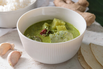 Bowl of tasty green chicken curry and ingredients on light background, closeup