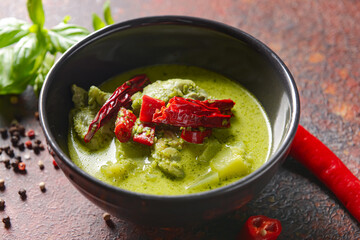 Bowl of tasty green chicken curry and ingredients on grunge background, closeup