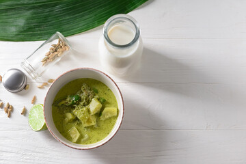 Bowl of tasty green chicken curry and ingredients on light wooden background