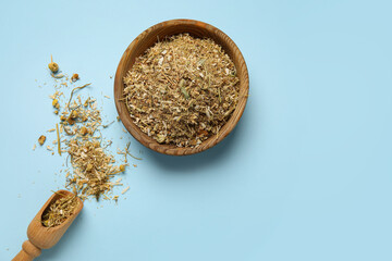 Bowl and scoop with dried chamomile flowers on color background
