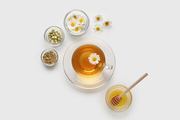 Composition with cup of chamomile tea, flowers and honey on light background