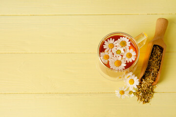 Cup of chamomile tea and scoop with dried flowers on color wooden background
