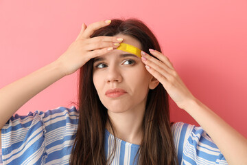 Displeased young woman with medical patch on her forehead against color background