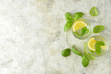 Glasses of tasty lemonade with basil on light background