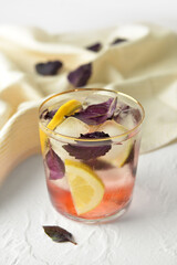 Glass of tasty lemonade with basil on light background