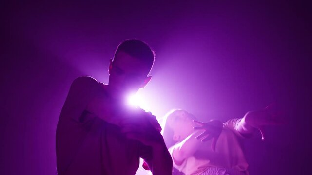 Professional young people choreographers dancing contemporary on dark background with pink light in studio. Talented dancers showing slow movements for dance music video, pair dance, duet. 