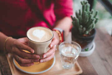 Female's hand holding cup of coffee on wooden table.