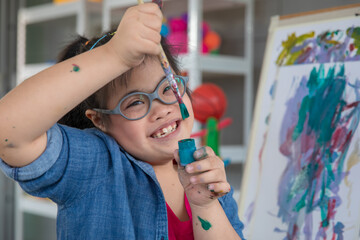 Happy girl with Down syndrome painting on easel