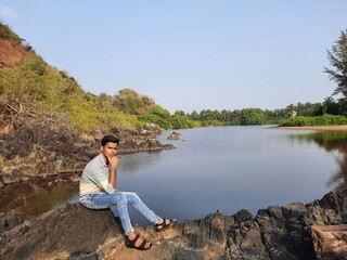 person sitting on a rock with beautiful lake in  background, a young men enjoying view of nature. Smiling pretty young man. 
