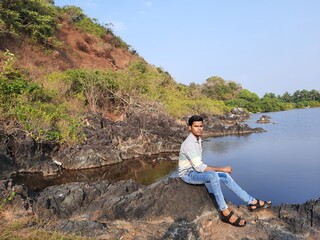 person sitting on a rock with beautiful lake in  background, a young men enjoying view of nature. Smiling pretty young man. 