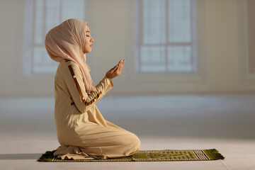 Beautiful Muslim woman in hijab dress sitting in mosque and praying