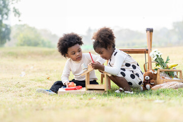 Two African American little boy and girl playing toy together in the park. Children with curly hair...