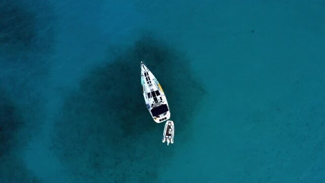 Sailboat With Inflatable Dinghy Floating On Clear Blue Sea Near The Bahamas In Caribbean. - aerial