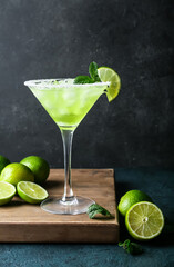 Glass of cold daiquiri cocktail and limes on dark background