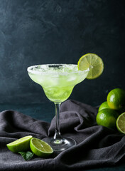 Glass of cold daiquiri cocktail and limes on dark background