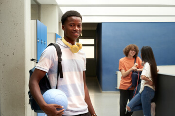 Portrait of an African American student looking at the camera in the school hallway and holding a ball.