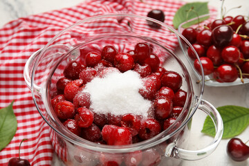 Glass pot with sweet cherry and sugar on light background, closeup