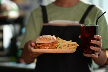 Woman holding tray of homemade burgers with fried potatoes and glass of soft drink.