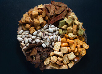 A snack for beer from different flavors of rusks and pistachios, laid out on a tree close-up. Dark background,view from above.