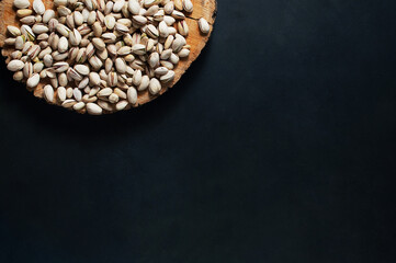 Pistachio nuts on a wooden stand. On a dark background, top view, horizontal orientation. Copy Space.