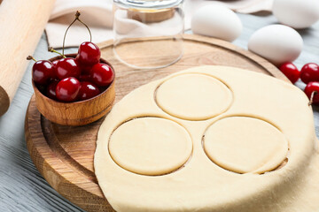 Board with fresh dough for cherry dumplings on color wooden background